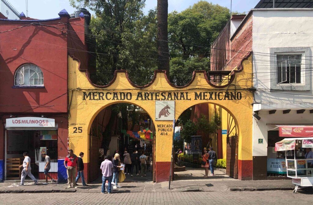 Yellow archway entrance to the Mercado Artesanal Mexicano with shoppers passing through in Coyoacán