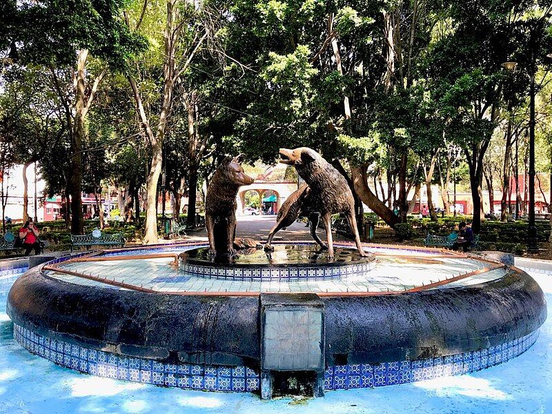 Bronze coyote fountain with blue tilework surrounded by trees at Jardín Centenario in Coyoacán