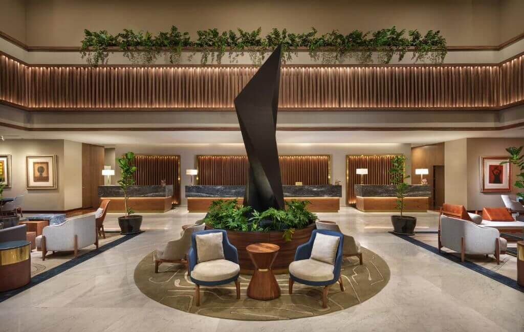 Spacious hotel lobby with a tall black sculpture, circular planter, lounge chairs, and hanging greenery at the Presidente InterContinental Mexico City