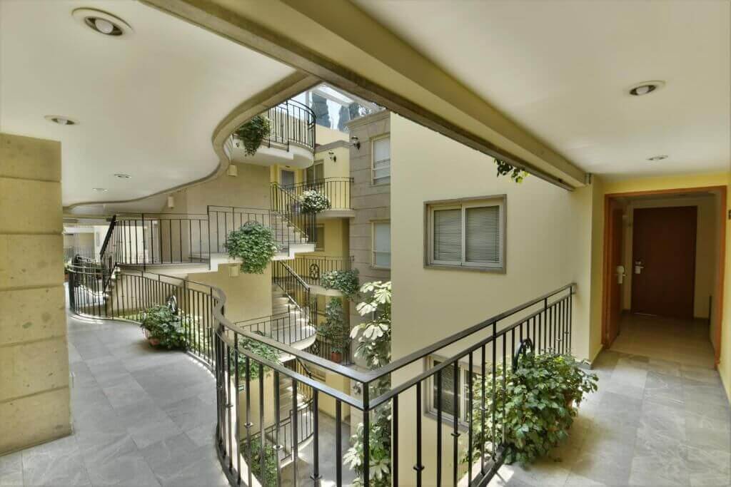 Open-air walkway with iron railings, potted plants, and a curving staircase in the interior courtyard at Suites Obelisk, Polanco